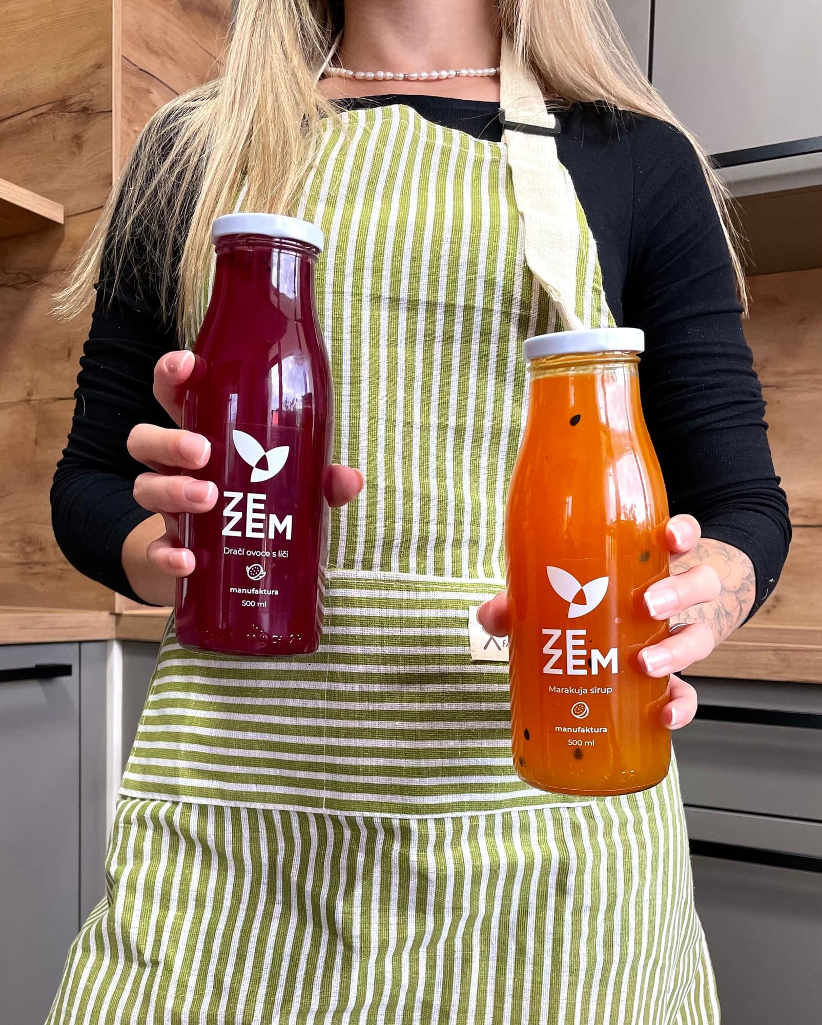 Zaměstnankyně ZEZEM v zástěře drží dvě láhve sirupu